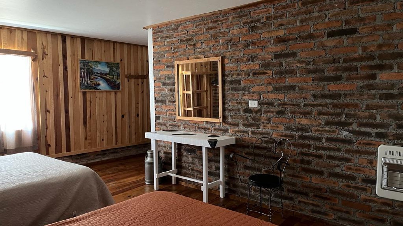 Lodge bedroom — wood paneling, exposed brick wall, landscape painting